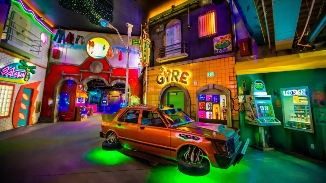 Colorful urban alley with neon lights; an orange car with glowing green lights; signs read