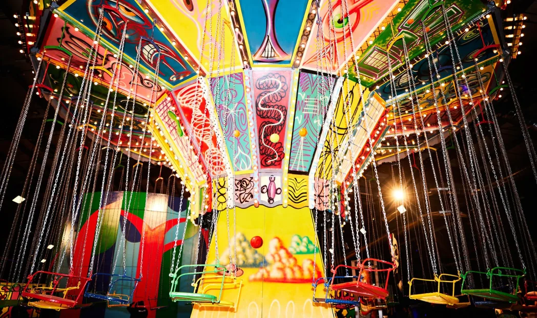 Colorful, empty swing ride with vibrant patterns and lights, set against a bright background, evoking a festive and playful atmosphere.